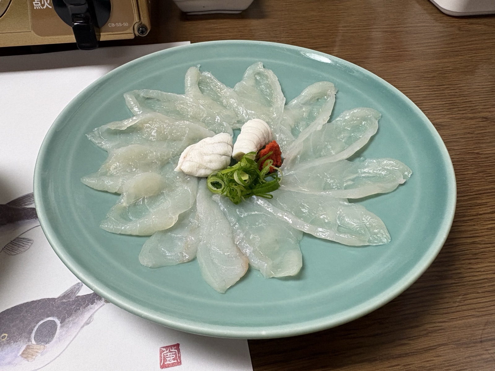 青磁の大皿に菊花のように盛り付けたてっさ。中央にふぐの湯引きと紅葉おろし、葱を添えて